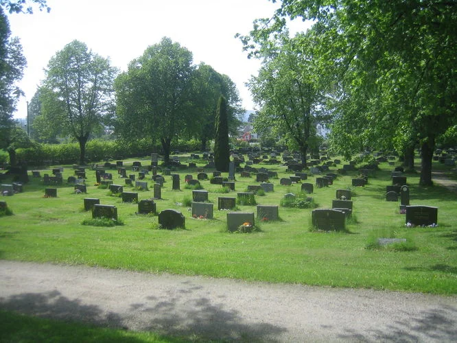 Gjerpen kirkegård med gravminner. Grønt grass og mange grønne trær. Foto.